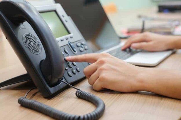 Employee multitasking by using their VoIP business phone and laptop for work.