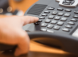 Close up of a VoIP system. An employee reaches to press a button the system.