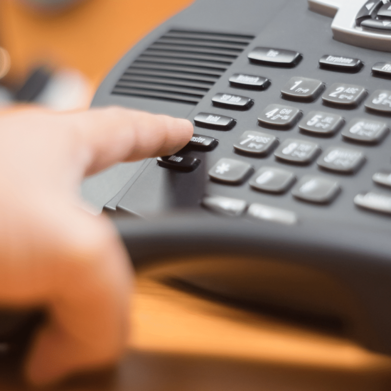 Close up of a VoIP system. An employee reaches to press a button the system.