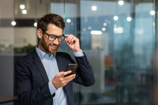 Businessman in business suit uses telephone near window.