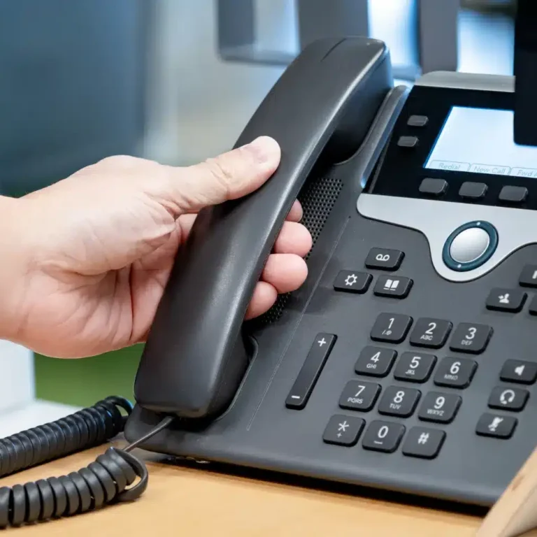 Blog Post Images-1 (4) A person's hand lifting the handset off a black office VoIP desk phone